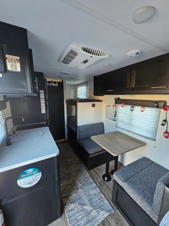 Bright RV rental interior showing a compact kitchen, dinette with grey seating, and bunk beds. Ideal for travel.. Forest River Cherokee Wolf Pup 2022