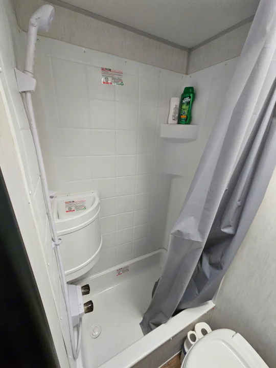 RV rental bathroom: compact white shower, handheld shower head, toilet, and gray curtain.. Forest River Cherokee Wolf Pup 2022