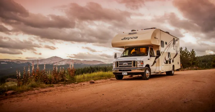 Jayco RV rental parked on a rustic dirt road, amidst mountains and tall plants under a dramatic sunset sky. Explore nature!. Jayco Redhawk 2016