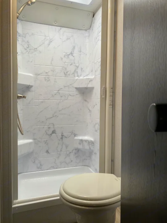 RV rental bathroom featuring a compact shower with marble-patterned walls, a hand-held shower, and a toilet in the shower area.. Forest River Sunseeker LE 2021