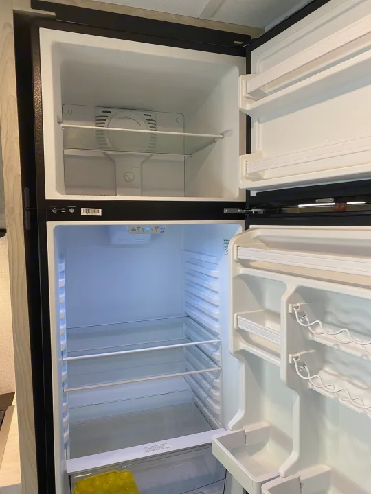 An open, empty two-door refrigerator/freezer in an RV rental, revealing interior shelves and temperature controls.. Forest River Sunseeker LE 2021
