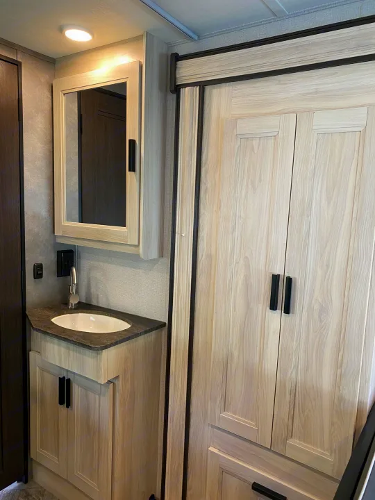 Modern RV rental bathroom featuring a light wood vanity, white sink, mirror, and tall storage cabinet, perfect for travel.. Forest River Sunseeker LE 2021