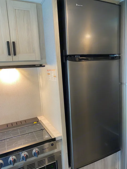 Modern RV rental kitchen with a stainless steel Magic Chef refrigerator and range, flanked by light-colored cabinets.. Forest River Sunseeker LE 2021