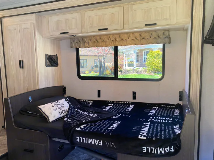 Inside an RV rental: a modern bedroom with a comfortable bed, overhead cabinets, and a window view.. Forest River Sunseeker LE 2021