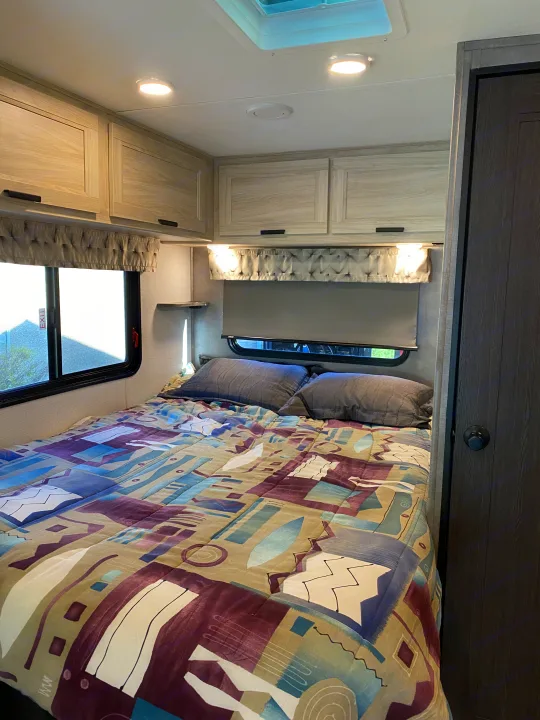 Cozy RV rental bedroom featuring patterned bedding, light cabinets, and bright lighting.. Forest River Sunseeker LE 2021