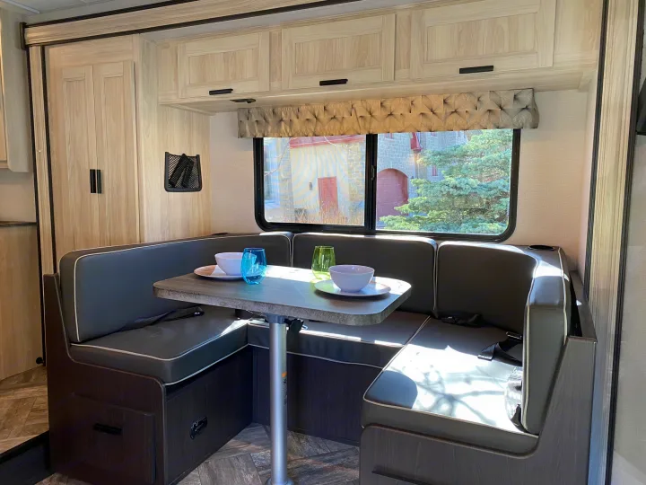 RV rental dinette with U-shaped seating, table set with colorful glasses, overhead cabinets, and a window view.. Forest River Sunseeker LE 2021