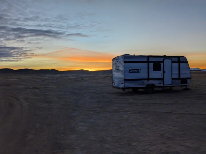 A Coleman **RV rental** parked in a vast, dim desert landscape at sunset, ideal for a peaceful outdoor escape.. Keystone Coleman 2025