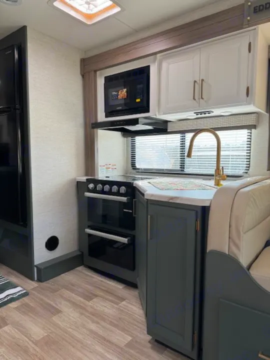 Modern RV rental kitchen featuring dark green cabinetry, full appliances, and a dinette area for comfortable travels.. Thor Eddie Bauer 28EB 2025