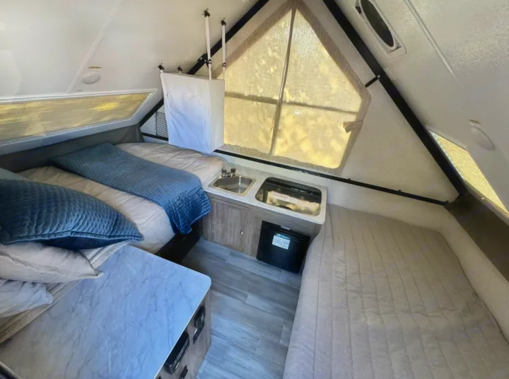 Interior of an RV rental: two beds (left & right), a central kitchenette with sink & stove, and storage. Ideal for travel.. Forest River Rockwood LTD 2023