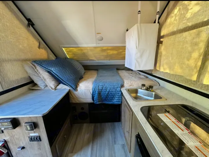 Compact RV rental interior featuring a cozy bed, kitchen with sink & stove, and control panel. Ideal for travel.. Forest River Rockwood LTD 2023
