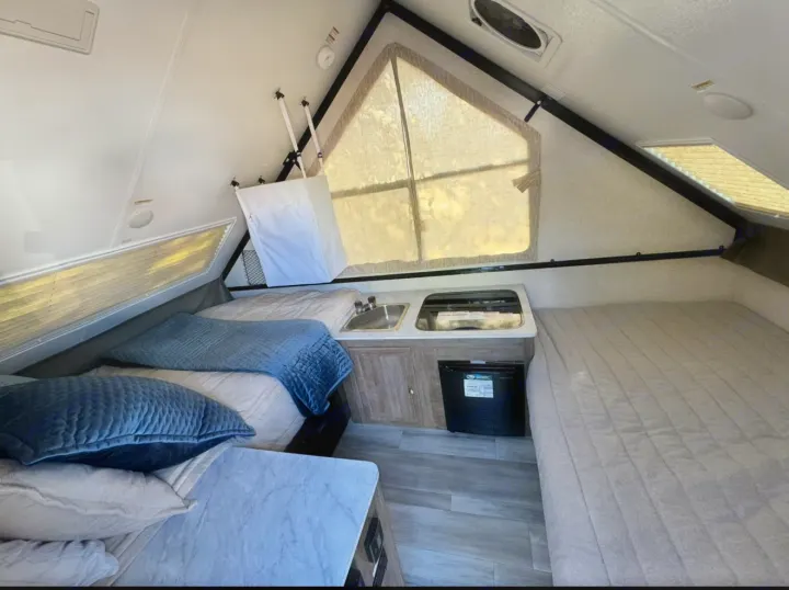 RV rental interior: A-frame camper with two beds, kitchenette, and mini-fridge for compact travel.. Forest River Rockwood LTD 2023