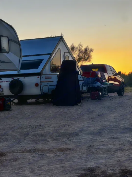 An RV rental A-frame camper and truck are set up for camping at sunset on a sandy site. Relaxing outdoor escape.. Forest River Rockwood LTD 2023