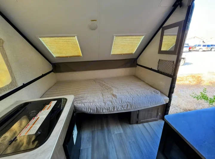 RV rental interior: A cozy bed, two skylights, and a compact kitchen counter with integrated cooktop/sink. Ideal camper setup.. Forest River Rockwood LTD 2023