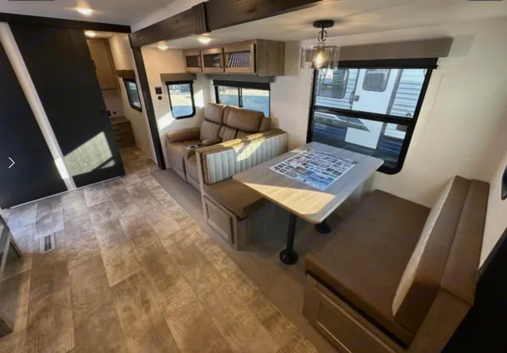 Bright RV rental interior showing a comfortable dinette, reclining sofa, and wood-look floor, ideal for travel.. Palomino Puma 337BH 2025