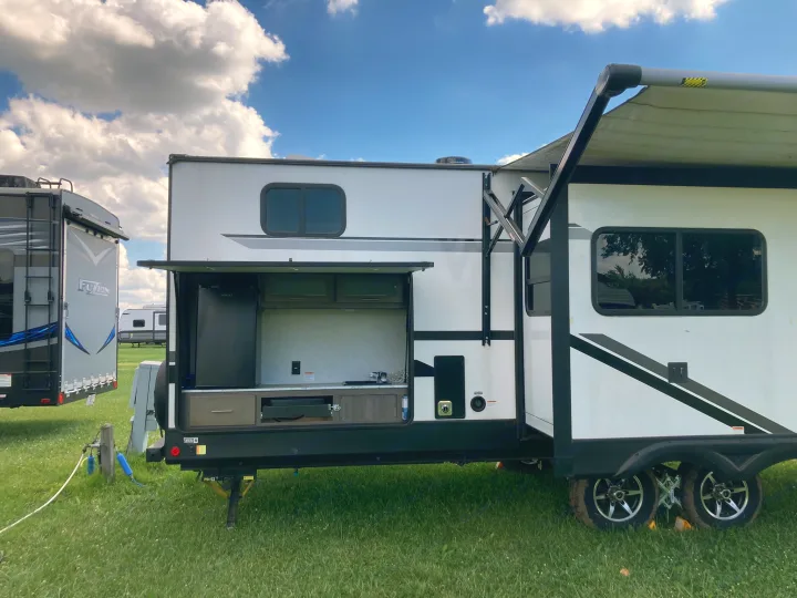 This modern white RV rental, parked on grass, features an open outdoor kitchen and extended awning.. Dutchmen Kodiak Ultimate 2020