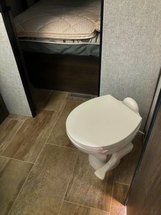 Inside an **RV rental**: a compact bathroom with a white toilet, showing the adjacent bed area and tiled floor for comfortable travel.. Dutchmen Kodiak Ultimate 2020