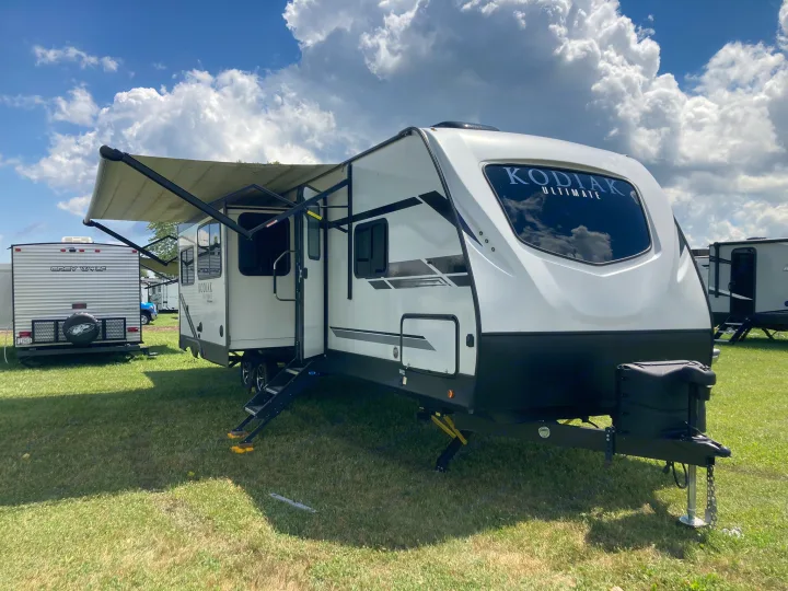 White Kodiak Ultimate travel trailer, perfect for an rv rental, set up outdoors on grass for camping.. Dutchmen Kodiak Ultimate 2020