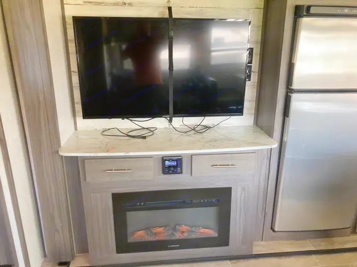 Modern RV rental living space featuring a TV, electric fireplace, refrigerator, and built-in audio system.. Dutchmen Kodiak Ultimate 2020