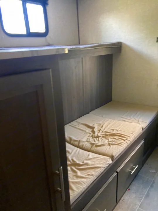 RV rental bunk beds with built-in storage drawers below and a window. Compact sleeping area in this camper interior.. Dutchmen Kodiak Ultimate 2020