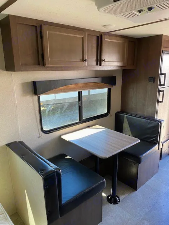RV rental dinette setup: two black benches, a table, and wood overhead cabinets. A comfortable and functional travel trailer space.. Sunset Park RV Sun Lite 2021