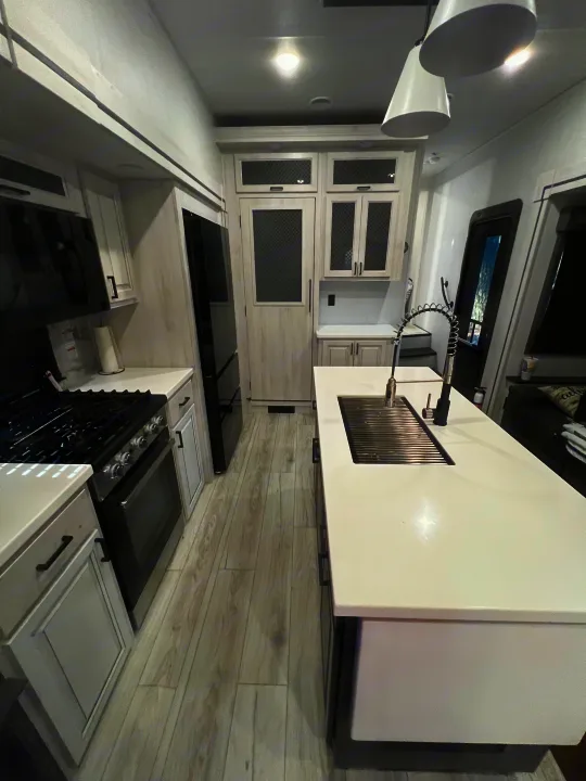 Experience comfort in this RV rental kitchen: white countertops, black appliances, island sink, and light flooring.. Forest River East to West Ahara 390DS 2025