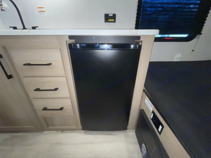 Inside this RV rental, find a compact kitchen with a built-in fridge, sink, and adjacent sleeping area, maximizing space.. Keystone RV Coleman 13B 2025