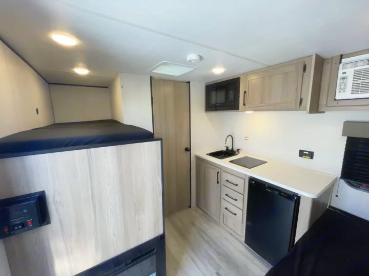 RV rental interior: modern kitchenette with sink, stove, microwave, fridge, and comfortable bunk beds.. Keystone RV Coleman 13B 2025