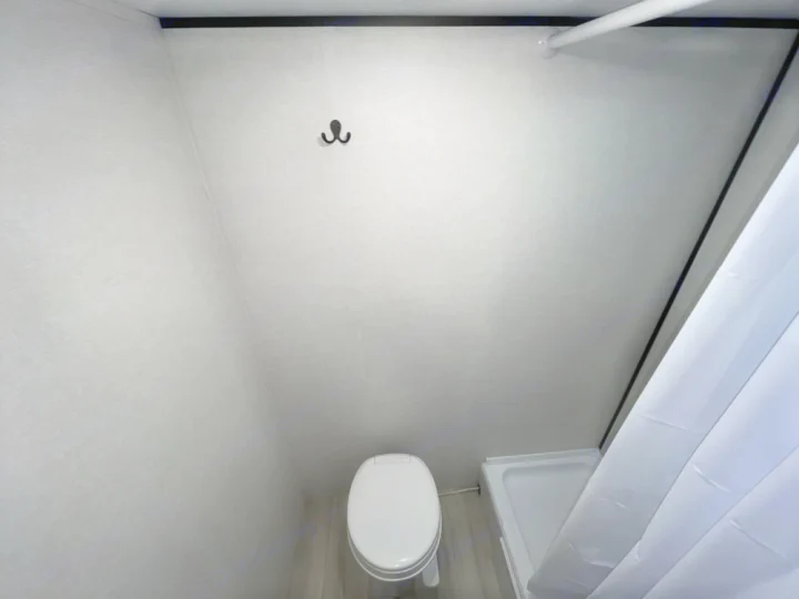 Inside an RV rental: a compact wet bath with a white toilet, small shower pan, and curtain. Walls are light gray.. Keystone RV Coleman 13B 2025