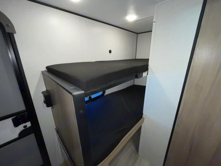 Interior of an RV rental: a neat sleeping area with black mattresses on built-in bunk beds. White walls and compact design.. Keystone RV Coleman 13B 2025