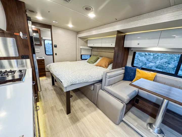 Spacious RV rental interior with a comfortable bed, modern kitchen, and dining lounge, perfect for your next road trip.. Winnebago Navion 2022