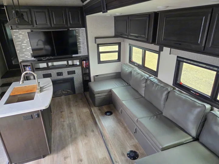 Spacious modern RV rental interior featuring a kitchen island, large sectional sofa, TV, and fireplace.. Open Range Highland Ridge 2021