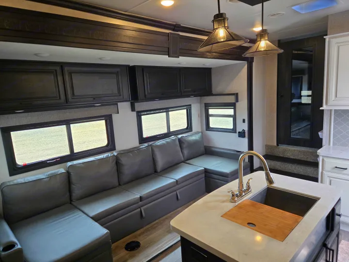 This inviting RV rental interior showcases a modern living area with a large sectional sofa, kitchen island, and ample light.. Open Range Highland Ridge 2021