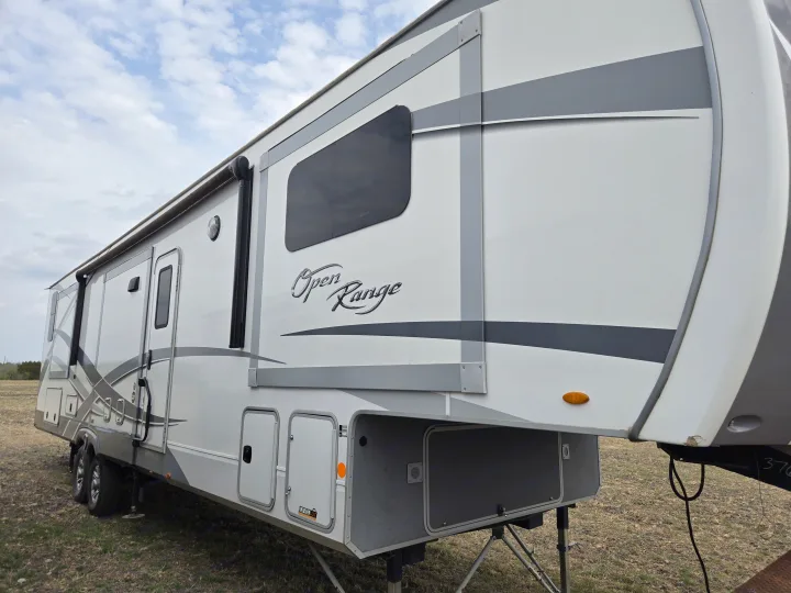 White and gray Open Range fifth-wheel RV rental, a spacious recreational vehicle parked on grass, ready for adventure.. Open Range Highland Ridge 2021