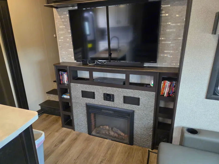 A modern RV rental living area with a dark wood entertainment center, large TV, built-in electric fireplace, and shelves.. Open Range Highland Ridge 2021