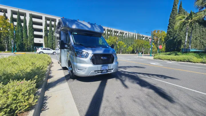 Modern silver RV rental (Tiffin) on a sunny street, with a large building and tall trees in the background.. Tiffin Motorhomes Allegro Midas 24MT 2024
