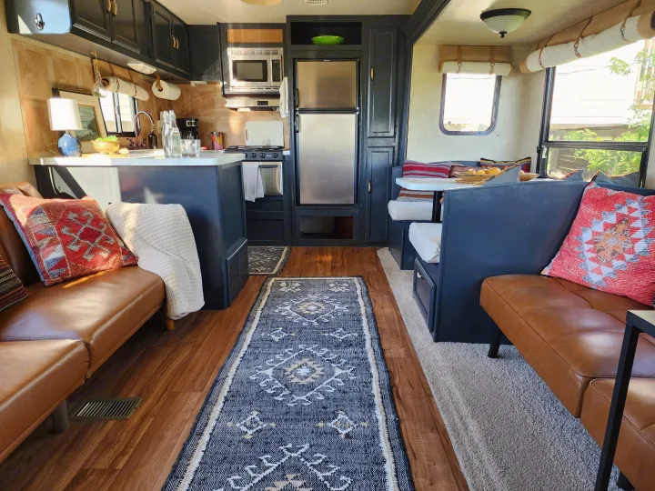 Modern RV rental interior: kitchen with dark cabinets, wood floors, cozy seating, and colorful pillows.. Forest River Wildwood 2017