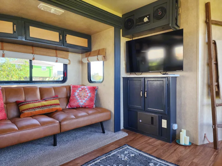 Comfortable RV rental living space with a brown sofa, colorful pillows, wall-mounted TV, and custom cabinetry.. Forest River Wildwood 2017