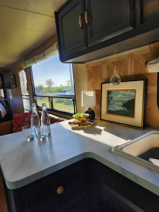 Cozy RV rental interior: sunlit kitchen counter with bottles, decor, sink, and a scenic window view.. Forest River Wildwood 2017