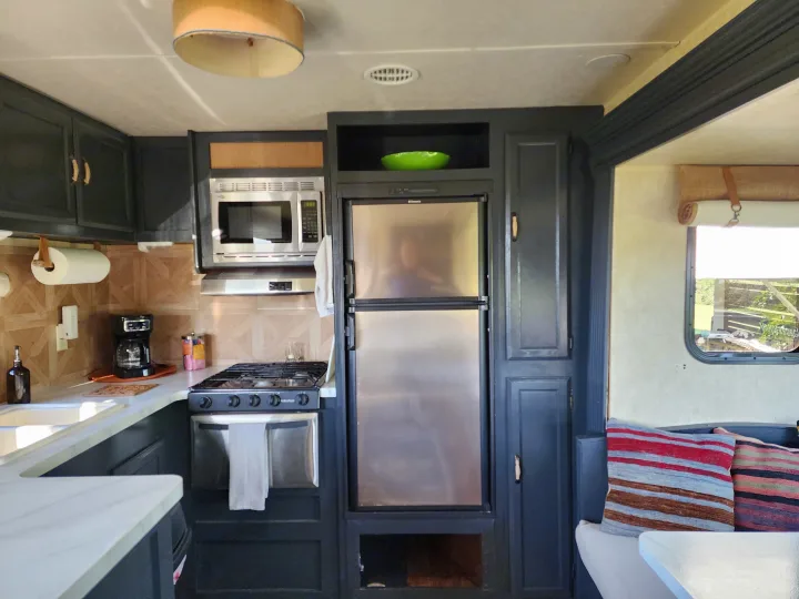 Modern RV rental kitchen featuring dark cabinetry, stainless appliances, white counters, and a dining nook.. Forest River Wildwood 2017