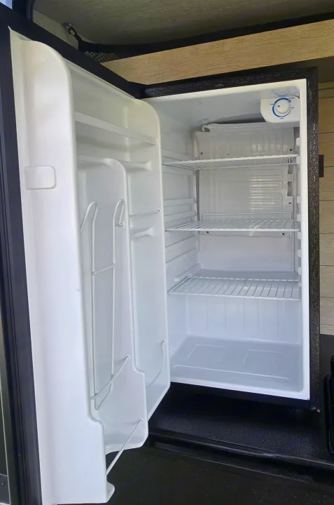 This RV rental features a clean, empty compact refrigerator with wire shelves and door storage, ready for your adventure.. Forest River Salem Platinum 2024