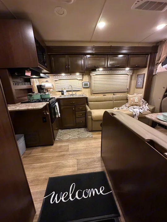 Explore this modern RV rental interior! Features a compact kitchen, lounge sofa, and dining setup for comfortable travel.. Thor Four Winds 2018