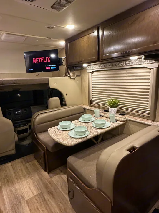 Cozy RV rental interior featuring a dining area, overhead Netflix TV, and a front bunk bed, ready for your next trip.. Thor Four Winds 2018
