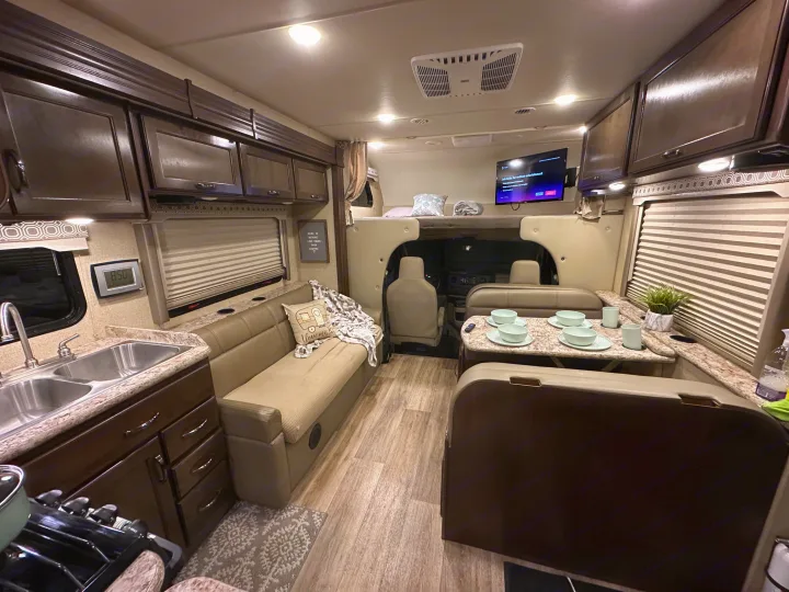 Cozy RV rental interior, bright and inviting, featuring a kitchen, dinette, and overhead bunk bed setup.. Thor Four Winds 2018