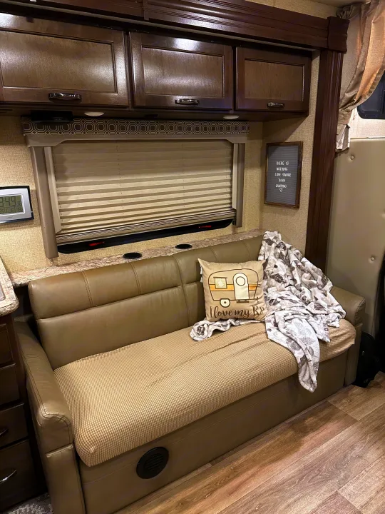 Cozy RV rental living space with a plush sofa, "I love my RV" pillow, overhead cabinets, and a window for camping comfort.. Thor Four Winds 2018