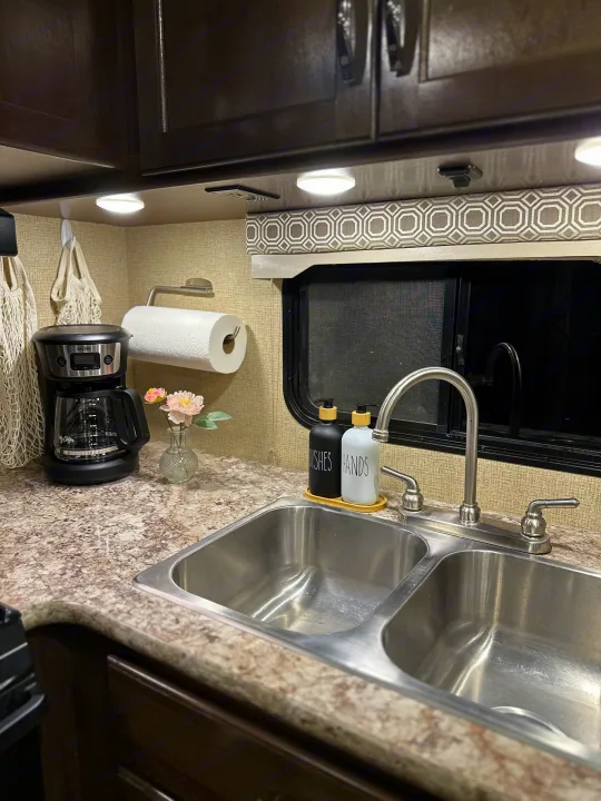 This RV rental kitchen features a dual sink, Mr. Coffee maker, and organized counter space with paper towels.. Thor Four Winds 2018