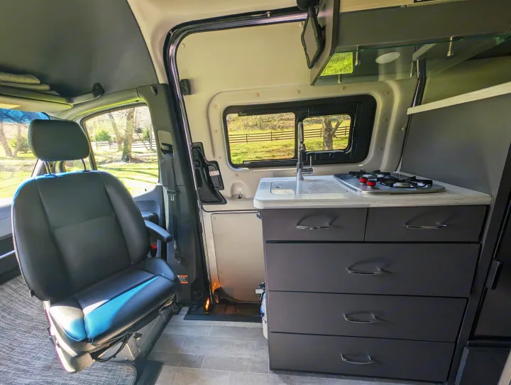Inside an RV rental: features include a modern kitchen with sink/stovetop & swiveling passenger seat, ready for adventure.. Thor Sanctuary 2021