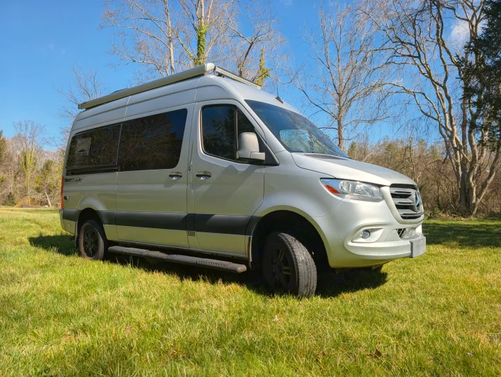 Silver Mercedes Sprinter RV rental parked on vibrant green grass under a clear blue sky, ideal for outdoor adventures.. Thor Sanctuary 2021