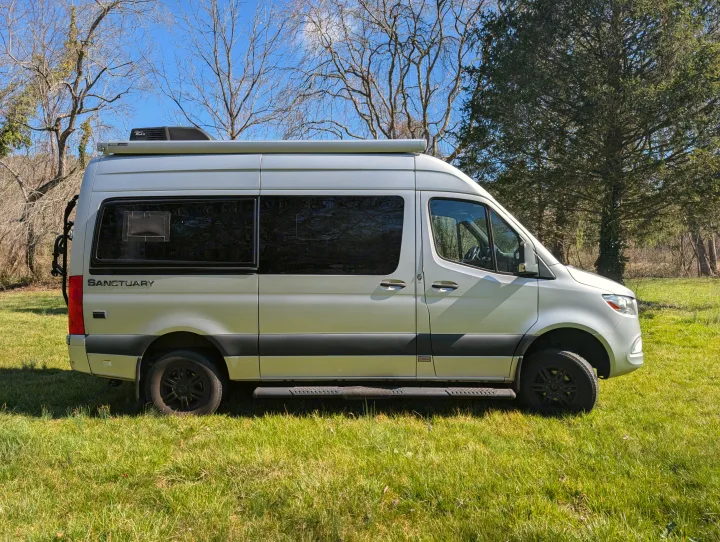 Silver Sanctuary camper van with awning & AC, parked on green grass. Perfect for an rv rental adventure.. Thor Sanctuary 2021