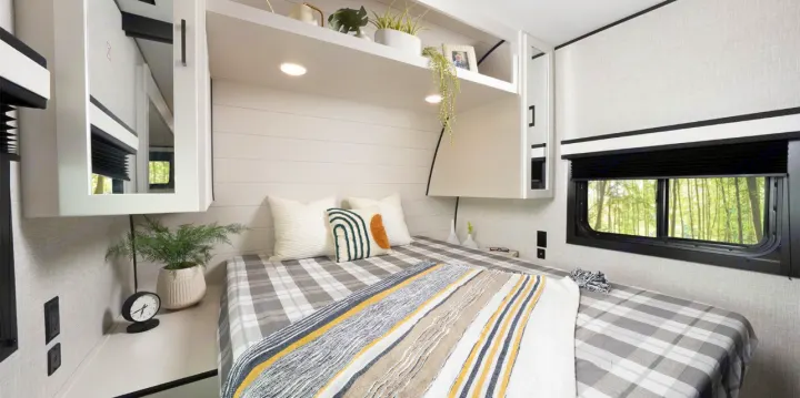 This RV rental's inviting bedroom offers plaid bedding, minimalist decor, and practical storage, creating a cozy travel space.. Jayco Jay Flight 261BHS 2025