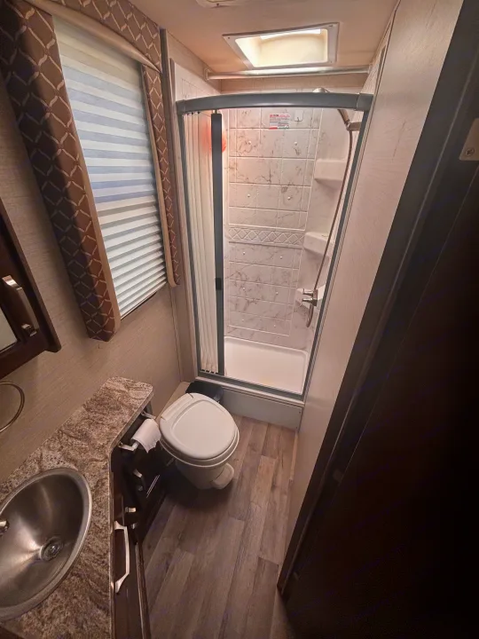 Compact RV rental bathroom with sink, toilet, and curved shower.. Jayco Melbourne 2020
